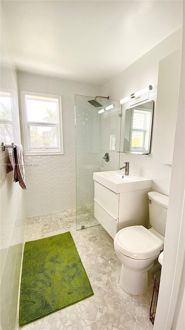 bathroom with tile floors, vanity, toilet, and tiled shower