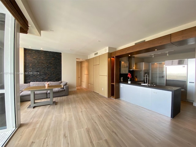 kitchen with wall chimney exhaust hood, stainless steel built in fridge, light hardwood / wood-style floors, and sink