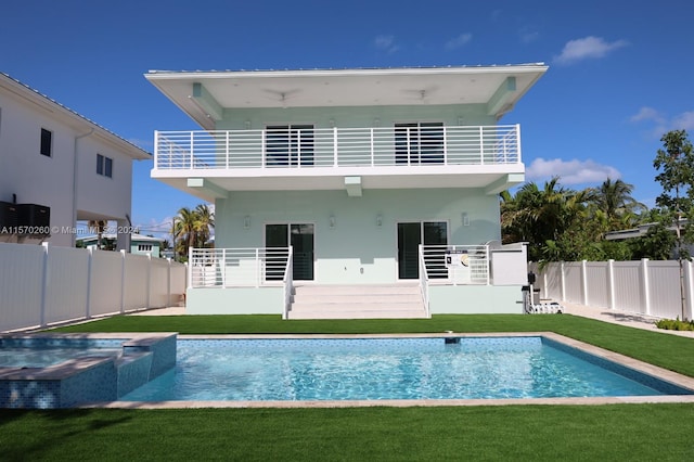 rear view of house with a balcony, a yard, and a fenced in pool