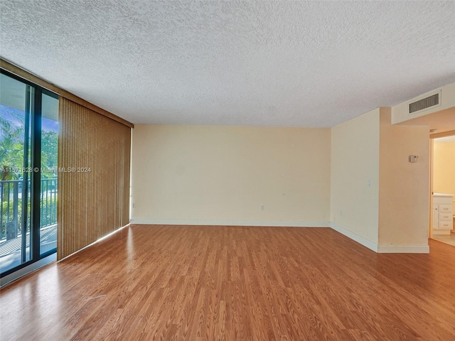 spare room with light hardwood / wood-style floors, a wall of windows, and a textured ceiling