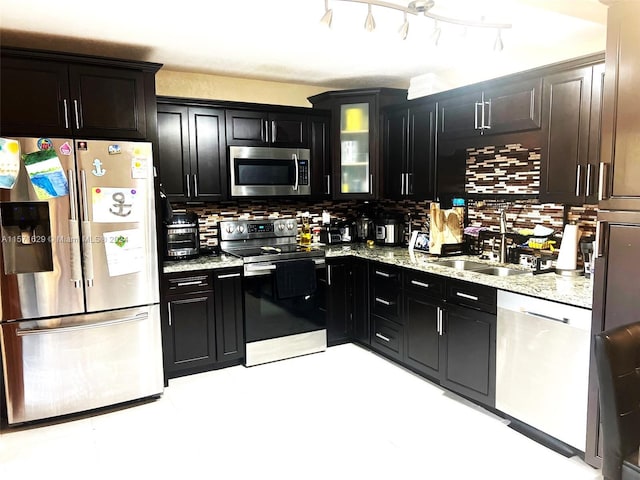 kitchen featuring stainless steel appliances, sink, light stone counters, decorative backsplash, and rail lighting