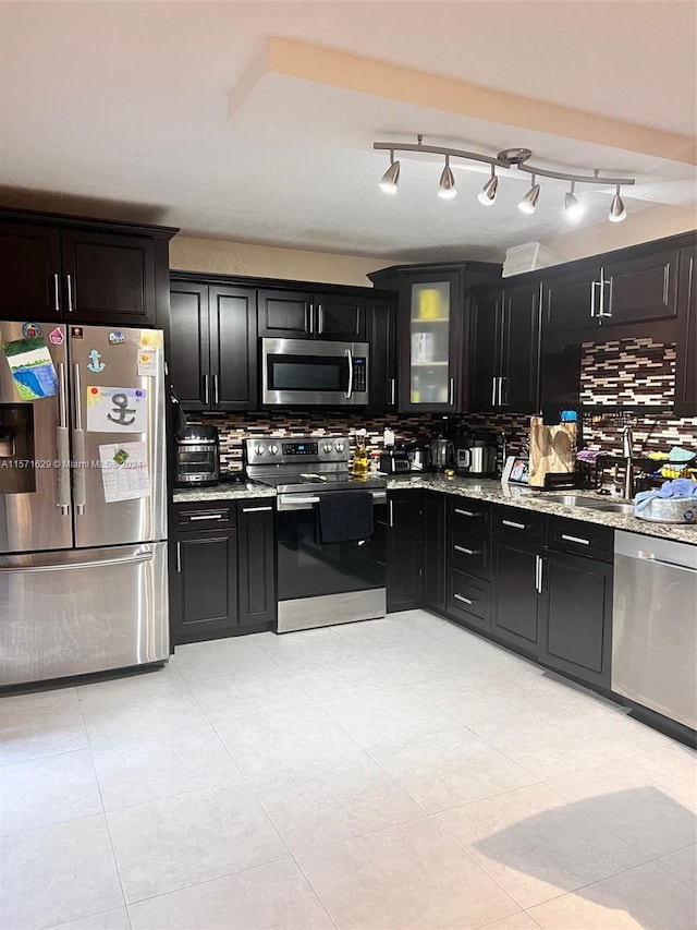 kitchen featuring light tile patterned flooring, stainless steel appliances, rail lighting, light stone counters, and backsplash