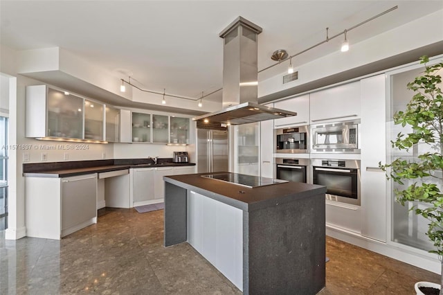 kitchen with island exhaust hood, white cabinetry, built in appliances, a center island, and track lighting