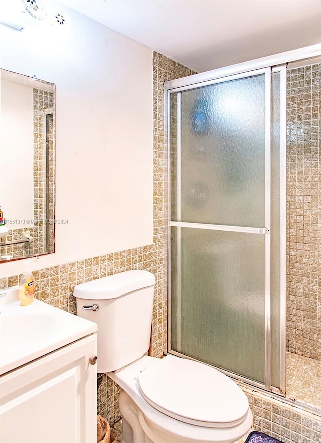 bathroom with tile walls, vanity, toilet, and a shower with shower door