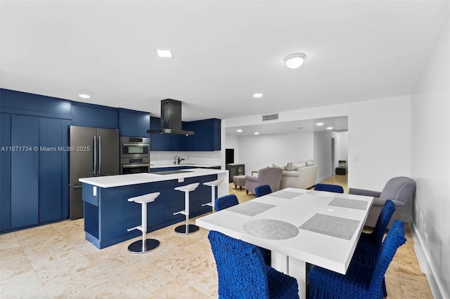 kitchen featuring wall chimney range hood, sink, a kitchen island, a kitchen bar, and stainless steel appliances