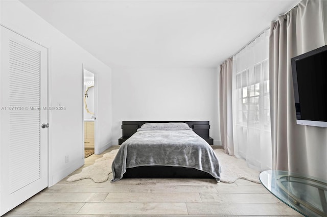 bedroom featuring connected bathroom and light hardwood / wood-style flooring