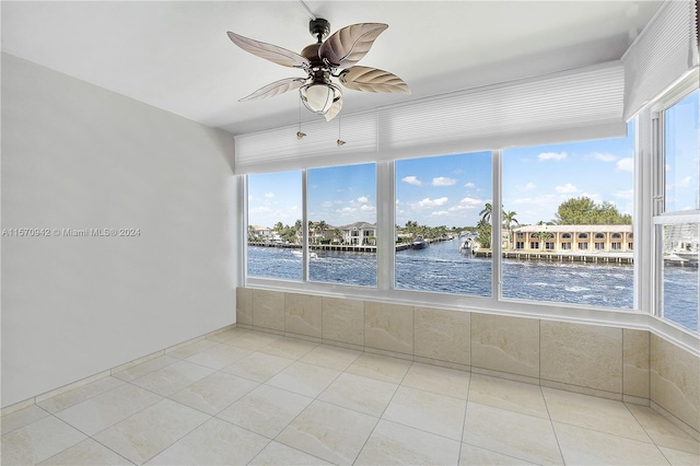 unfurnished sunroom featuring ceiling fan and a water view