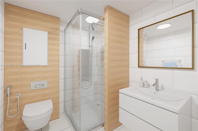 bathroom with vanity, toilet, a shower with shower door, and tile walls