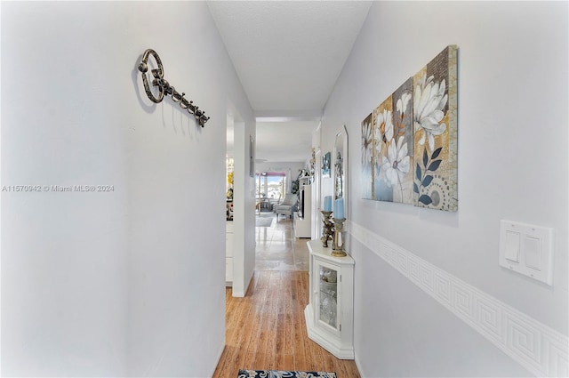 hallway with a textured ceiling and light hardwood / wood-style flooring