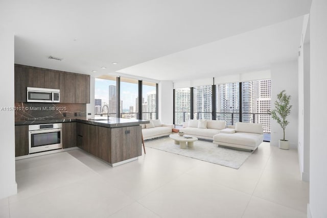 kitchen with dark countertops, open floor plan, a peninsula, stainless steel appliances, and a city view