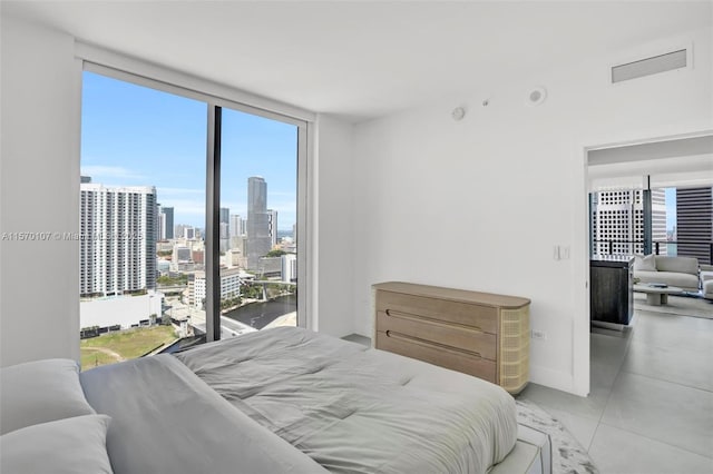 bedroom with a wall of windows, a view of city, visible vents, and light tile patterned floors