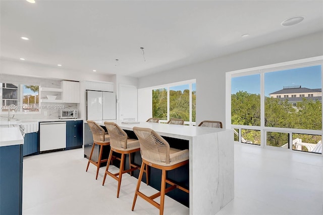 kitchen featuring backsplash, a kitchen breakfast bar, white cabinets, and white appliances