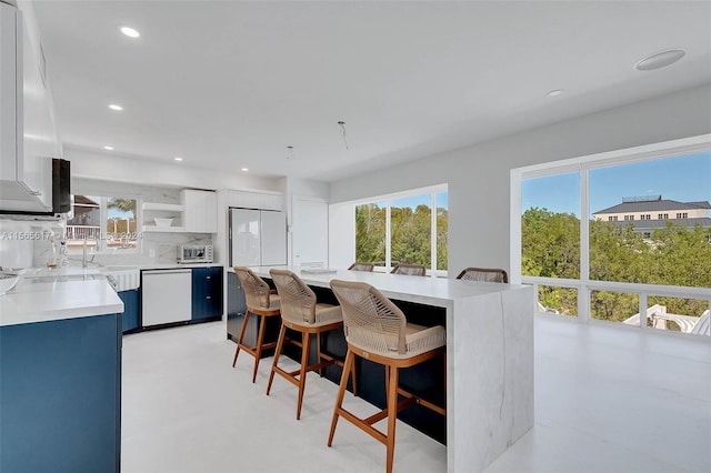 kitchen with tasteful backsplash, white cabinetry, a breakfast bar area, and white appliances