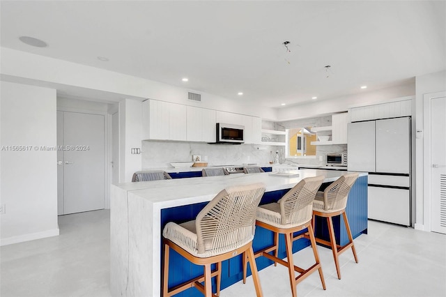 kitchen featuring white cabinets, a kitchen bar, tasteful backsplash, built in refrigerator, and light stone countertops