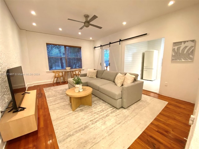 living room featuring a barn door, dark hardwood / wood-style flooring, and ceiling fan