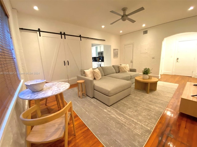 living room featuring ceiling fan, light wood-type flooring, and a barn door