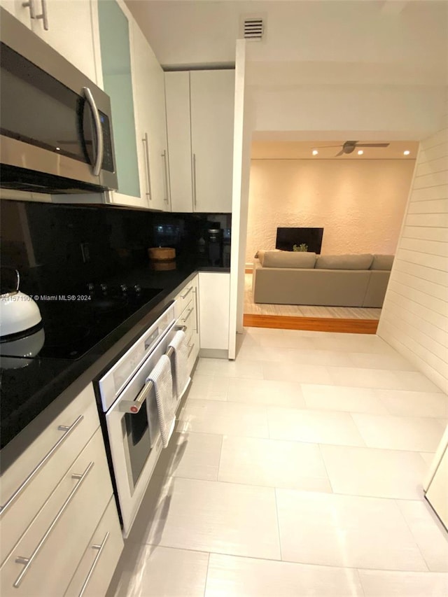 kitchen featuring appliances with stainless steel finishes, light tile flooring, backsplash, and white cabinetry