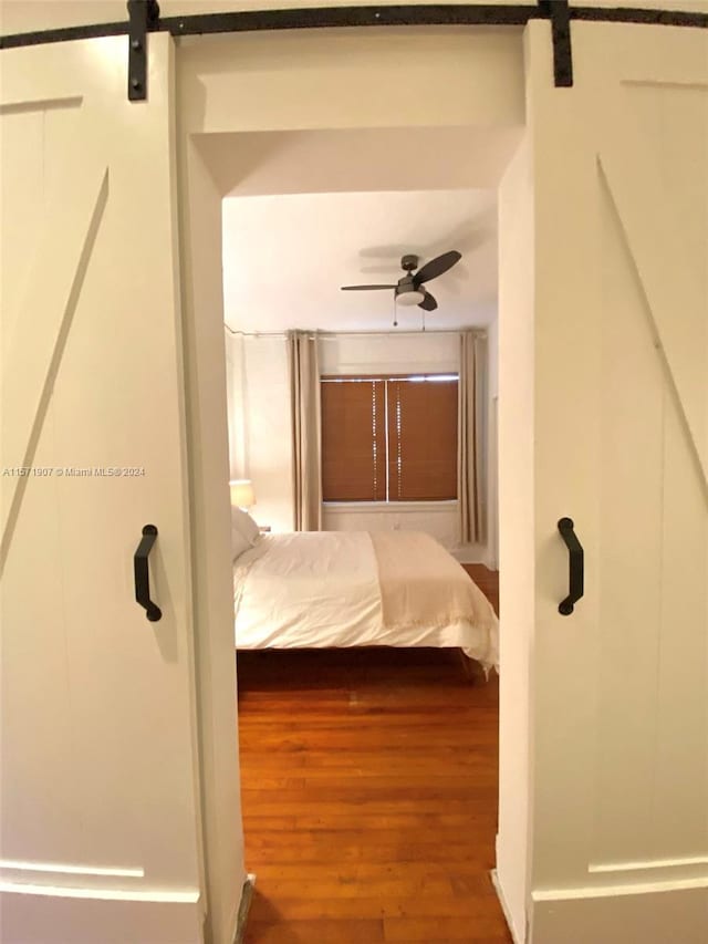 unfurnished bedroom featuring a barn door, dark hardwood / wood-style flooring, and ceiling fan