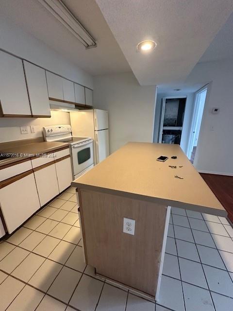 3985 W Mcnab Rd Unit A111, Pompano Beach, FL 33069 - kitchen featuring electric range, white cabinets, light tile patterned floors, a center island, and light countertops