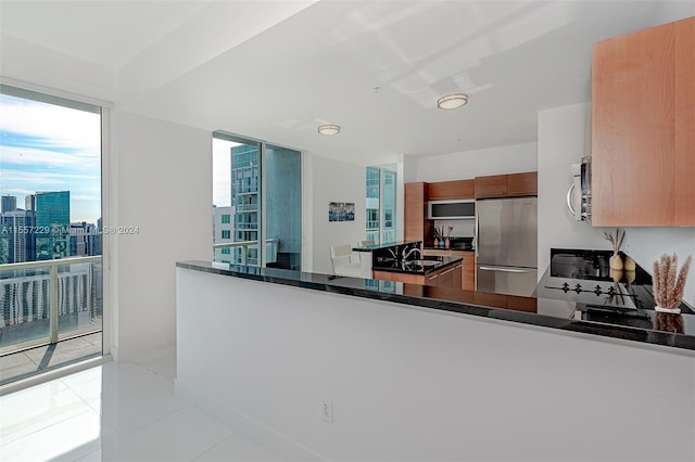 kitchen featuring appliances with stainless steel finishes, kitchen peninsula, light tile floors, and dark stone countertops