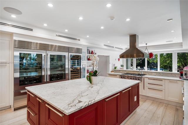 kitchen featuring island exhaust hood, appliances with stainless steel finishes, light wood-type flooring, light stone counters, and a kitchen island