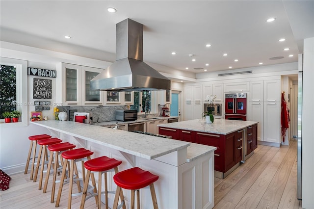 kitchen with a center island, stainless steel appliances, kitchen peninsula, a kitchen bar, and island range hood