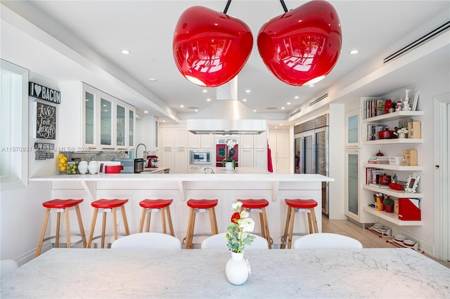 kitchen featuring a breakfast bar, white cabinets, built in appliances, kitchen peninsula, and island exhaust hood