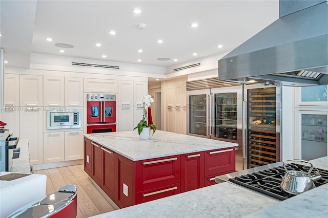 kitchen featuring appliances with stainless steel finishes, light stone counters, island range hood, light hardwood / wood-style flooring, and a center island