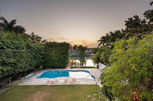 pool at dusk with a patio area, a yard, and a water view