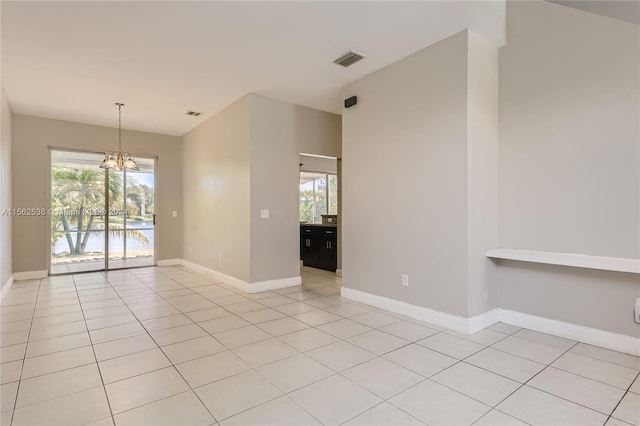 tiled empty room featuring a wealth of natural light and a notable chandelier