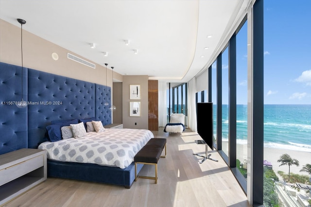 bedroom featuring floor to ceiling windows, a water view, a view of the beach, and light wood-type flooring