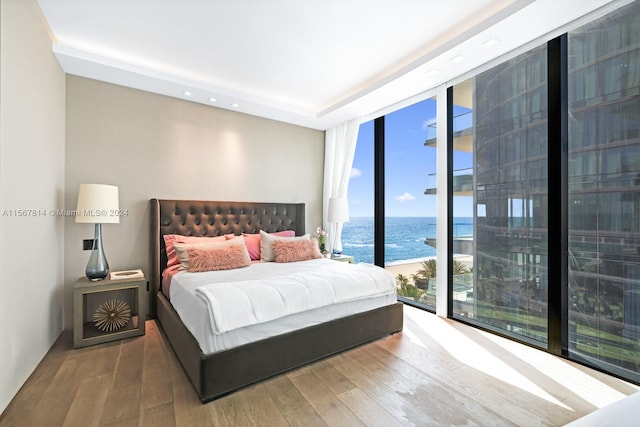 bedroom with a water view, wood-type flooring, and a wall of windows