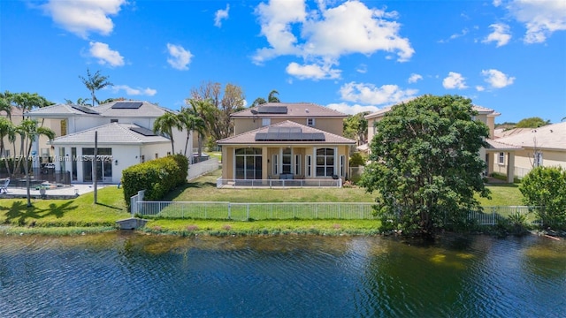 back of property featuring a yard, a water view, and solar panels