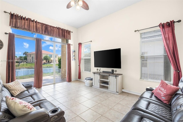 tiled living room with ceiling fan, a wealth of natural light, and a water view