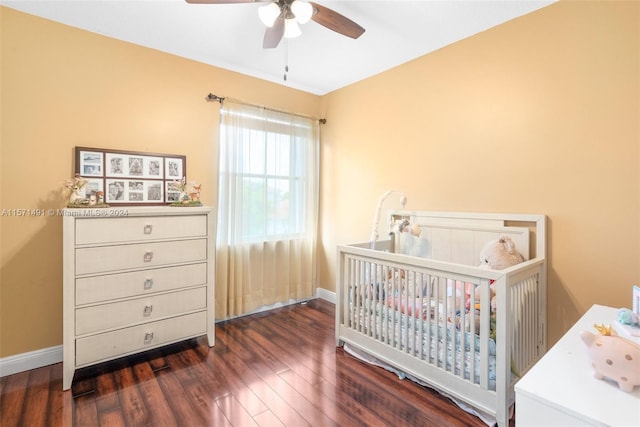 bedroom with a crib, dark hardwood / wood-style flooring, and ceiling fan