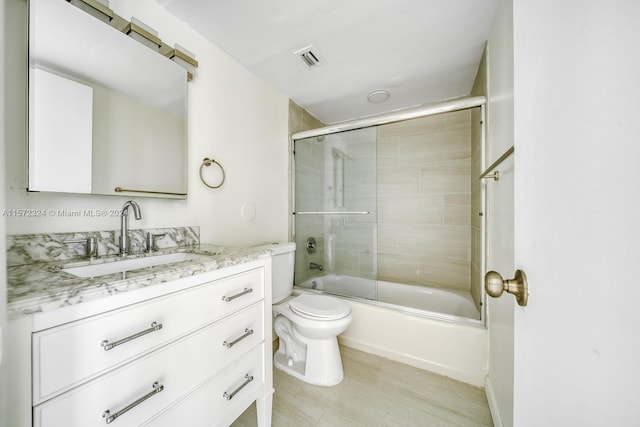 full bathroom featuring toilet, large vanity, and bath / shower combo with glass door