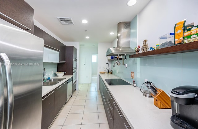 kitchen with appliances with stainless steel finishes, light tile floors, sink, island exhaust hood, and dark brown cabinetry