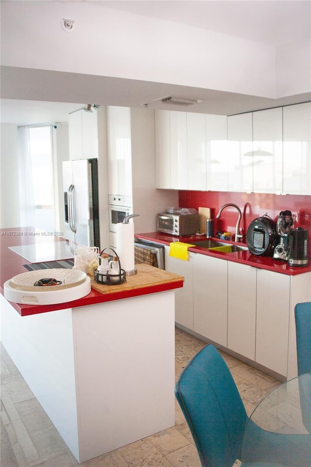 kitchen featuring white oven, white cabinetry, a sink, and stainless steel fridge with ice dispenser