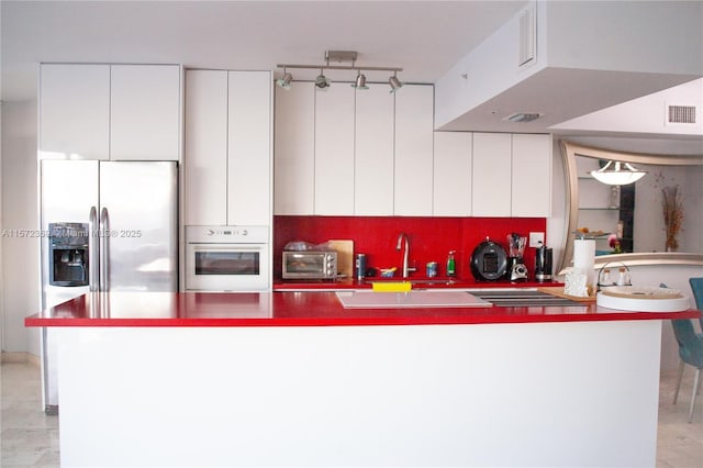 kitchen featuring visible vents, stainless steel fridge with ice dispenser, white oven, white cabinetry, and a sink