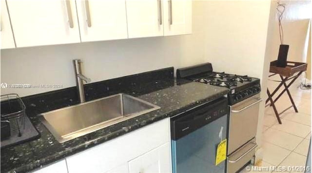 kitchen with dark stone counters, white cabinets, gas range, dishwasher, and light tile floors