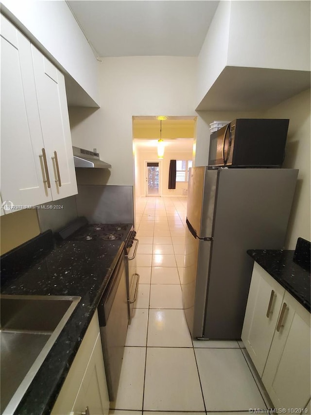 kitchen featuring stainless steel refrigerator, light tile flooring, white cabinetry, dark stone countertops, and sink