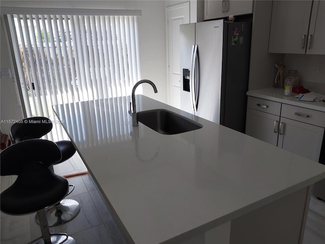 kitchen featuring stainless steel fridge with ice dispenser, sink, light tile flooring, and a kitchen island