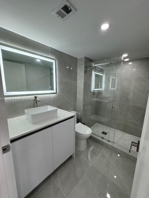 bathroom featuring tile walls, toilet, tile floors, vanity, and a shower with door