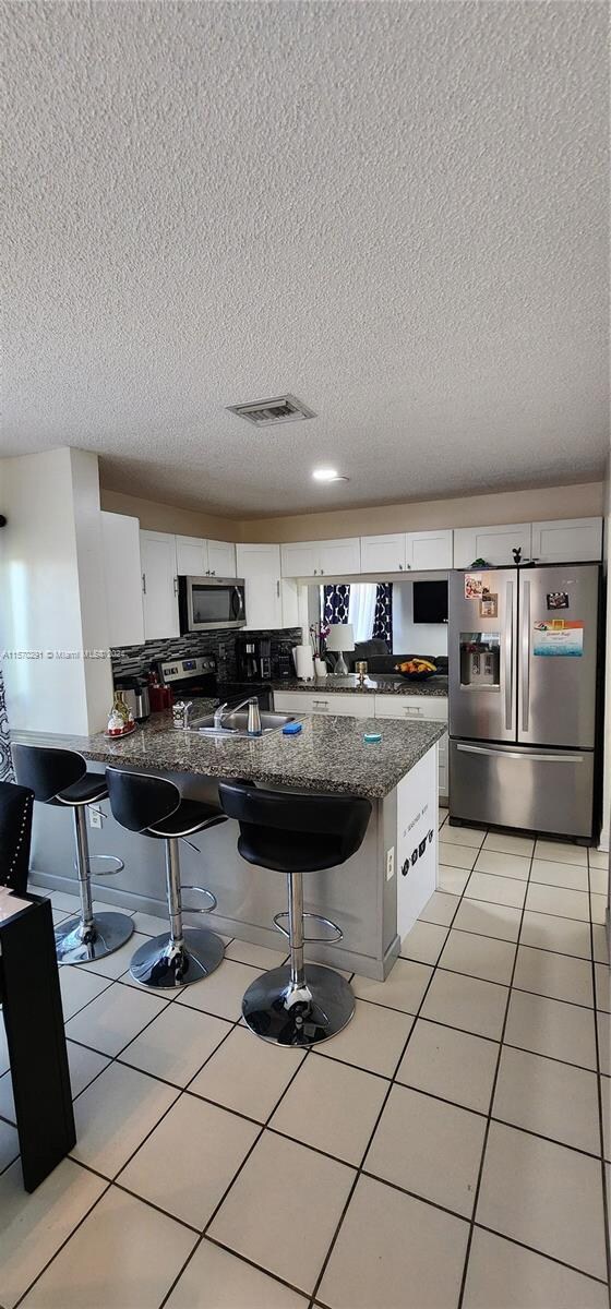 kitchen with appliances with stainless steel finishes, a kitchen breakfast bar, white cabinets, and a textured ceiling