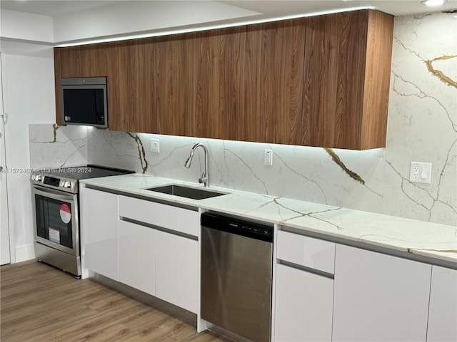 kitchen with light stone counters, sink, light hardwood / wood-style floors, backsplash, and stainless steel appliances