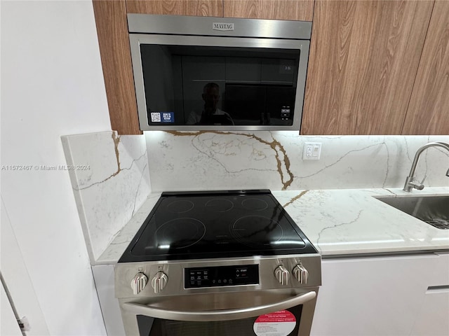 kitchen with appliances with stainless steel finishes, sink, backsplash, and light stone counters