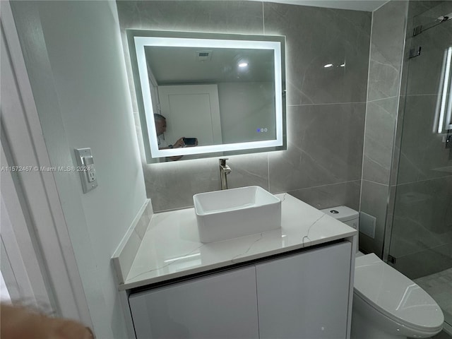 bathroom with vanity, toilet, tiled shower, and tile walls