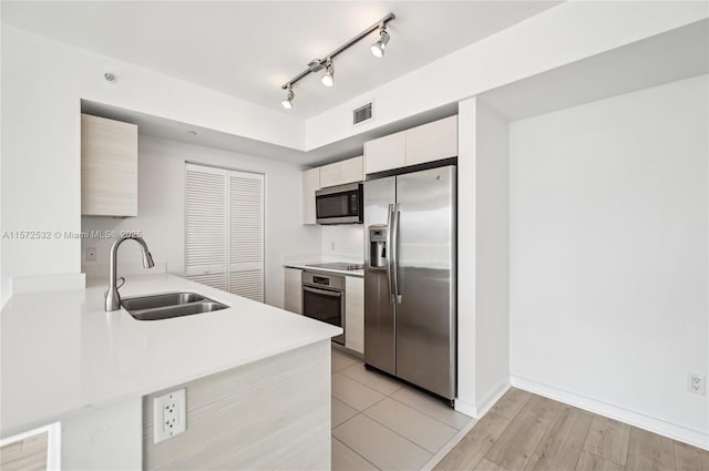 kitchen featuring sink, kitchen peninsula, light wood-type flooring, white cabinetry, and stainless steel appliances