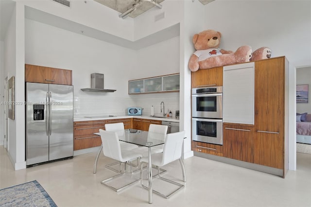 kitchen with tasteful backsplash, wall chimney exhaust hood, stainless steel appliances, a high ceiling, and sink