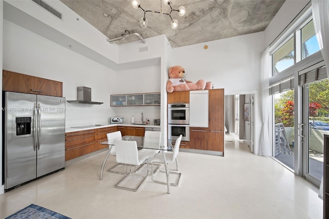 kitchen featuring sink, wall chimney range hood, a kitchen breakfast bar, backsplash, and appliances with stainless steel finishes